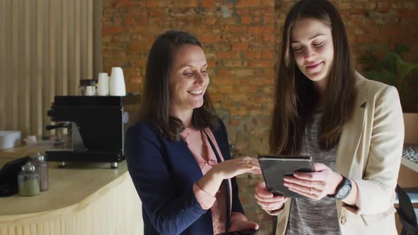 Caucasian female business owner and her coworker using tablet and talking alt