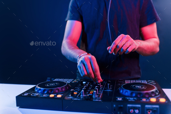 Close up view of DJ\'s hands that working with music equipment in the club with neon lighting