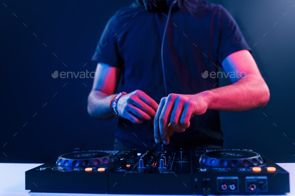 Close up view of DJ\'s hands that working with music equipment in the club with neon lighting