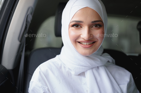 Beautiful muslim woman in white hijab sitting on the back seat of a luxury car