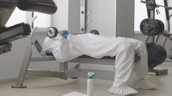 Wide Shot of Woman in White Protective Suit, Eyeglasses and Respirator Lying on Sport Bench and alt