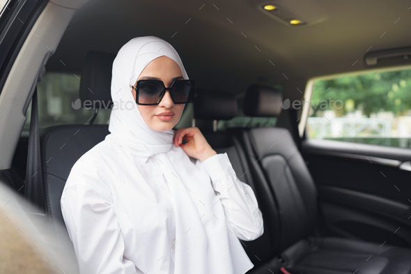 Beautiful muslim woman in white hijab sitting on the back seat of a luxury car