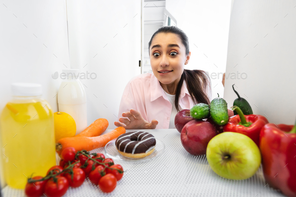 Excited funny woman looking at yummy donut view from fridge