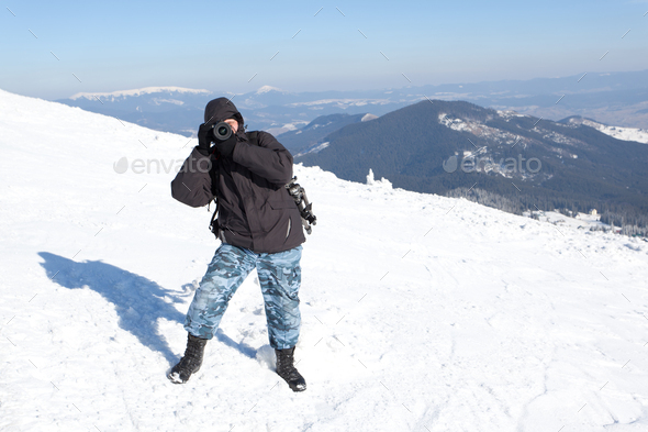 Photographer standing with camera on hill with panoramic view of winter valley