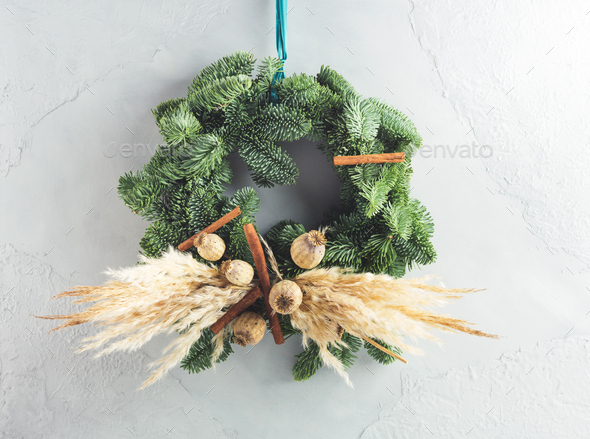 Christmas natural spruce wreath with dry decor, pampas reed and cinnamon over gray wall background