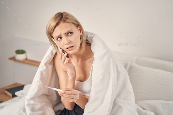 Upset woman with a thermometer sitting in bed