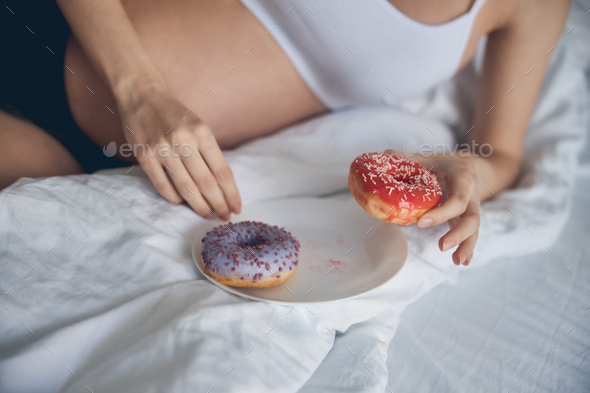 Sweet pink and violet donut on the white bed in hand of pregnant woman
