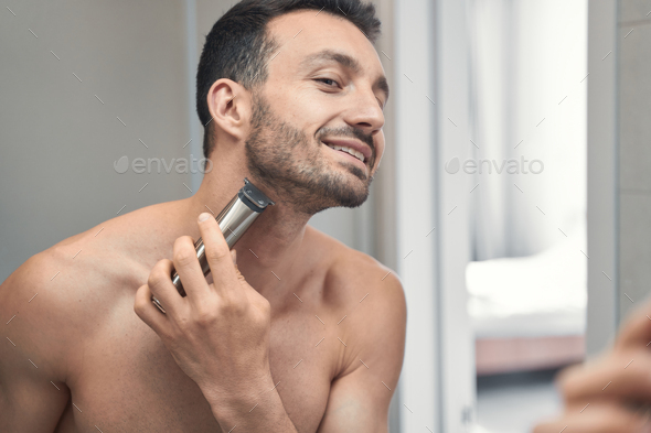 Smiling young man shaving face in front of the mirror