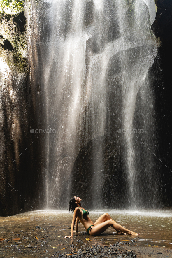 Pleased brunette girl sitting under the waterfall