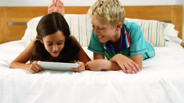 Siblings using digital tablet in bedroom alt