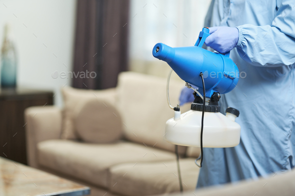 Worker wearing protective overalls while disinfecting a hotel apartment - Stock Photo - Images