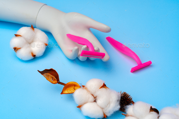 Pink disposable razors and cotton flower on blue paper