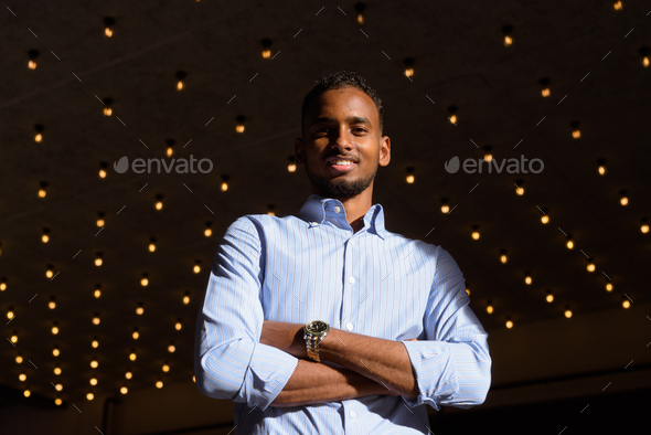 Low angle view shot of handsome black African businessman outdoors in city during summer smiling - Stock Photo - Images