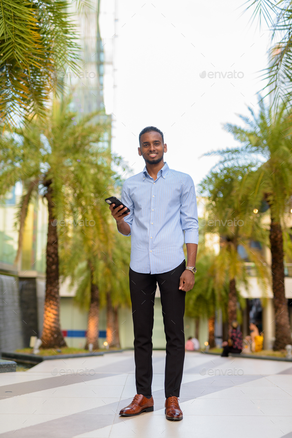 Full length shot of handsome black African businessman outdoors in city during summer smiling and - Stock Photo - Images