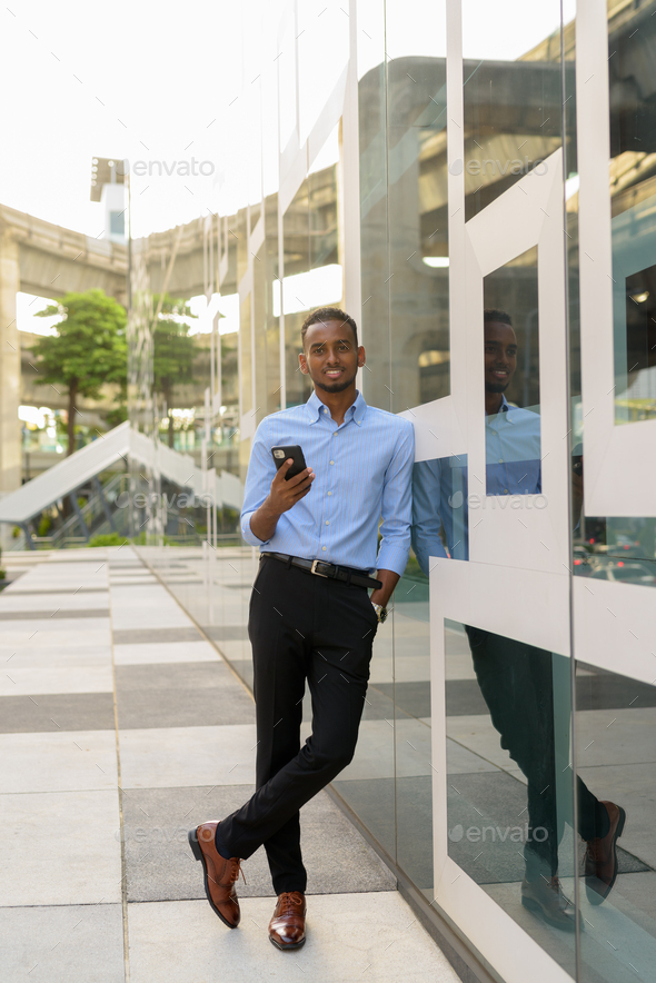 Full length shot of handsome black African businessman outdoors in city during summer smiling and - Stock Photo - Images