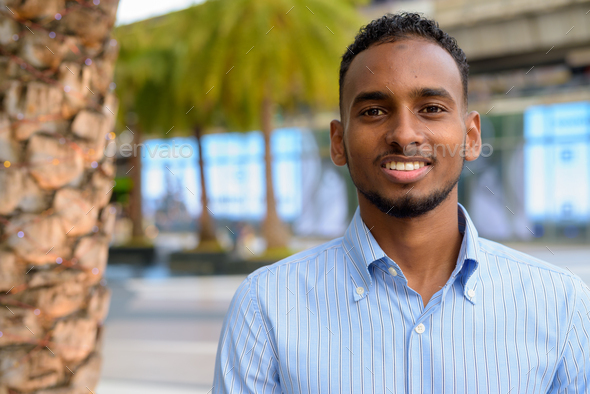 Portrait of handsome black African businessman outdoors in city during summer smiling - Stock Photo - Images