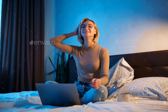 Blonde young girl working on computer in bed - Stock Photo - Images