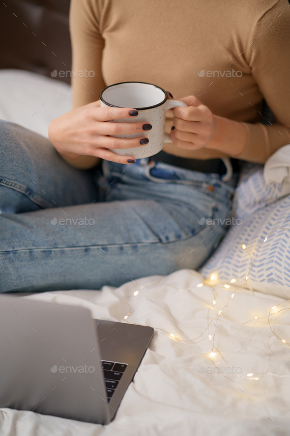 Woman holding a cup of coffee on bed - Stock Photo - Images