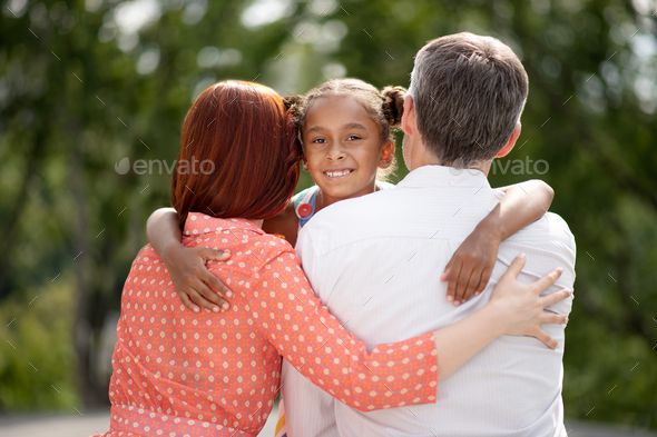 Dark-skinned girl feeling happy while hugging her foster parents