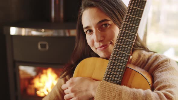 Portrait of Happy Woman with Guitar by Fireplace at Home alt