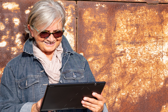 Attractive and modern elderly woman grey haired using digital tablet outdoor under the sun