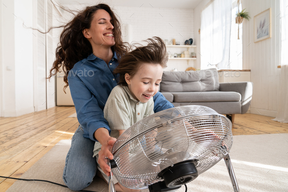 Family together: young mom and preschool son laugh sitting at ventilator blowing cool wind in face
