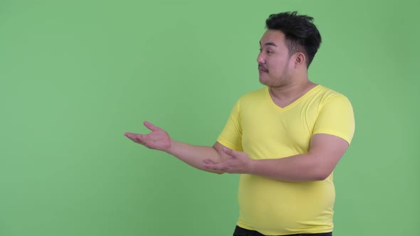 Happy Young Overweight Asian Man Talking While Showing Something alt