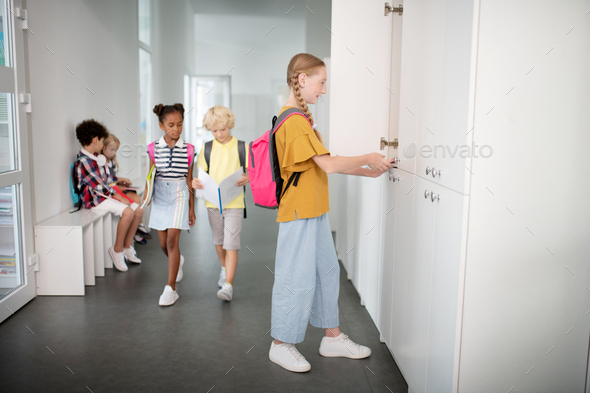 Girl with pink backpack standing near locker in the school hallway
