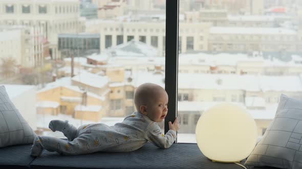 boy toddler lies on the windowsill by the window overlooking the city