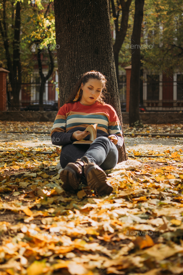 Young plus size woman reading book in fall autumn park in sun lights. Body positive, diversity, Body
