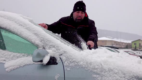 Man cleaning car windshield from snow and ice alt