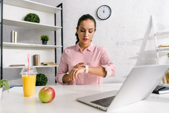 attractive girl looking at watch near laptop and apple - Stock Photo - Images