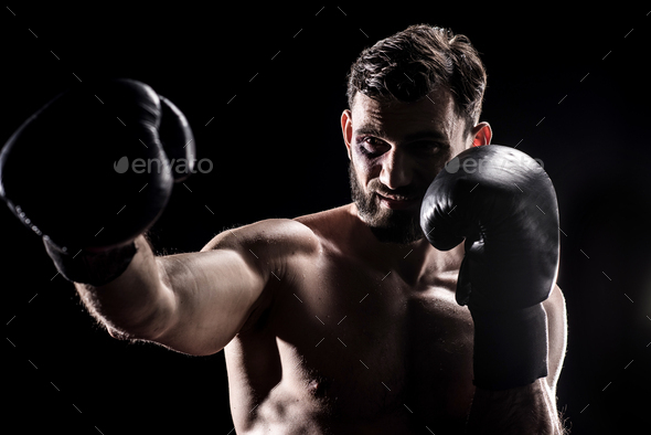 Young black eyed boxer in gloves punching the air isolated on black