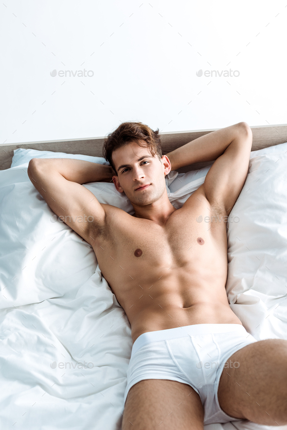 sexy young man in underwear lying on bed and looking at camera Stock Photo  by LightFieldStudios