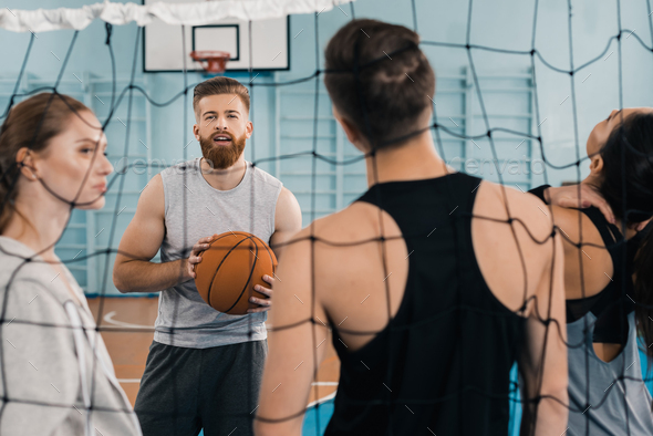 Bearded young sportsman with ball talking with teammates in sports hall