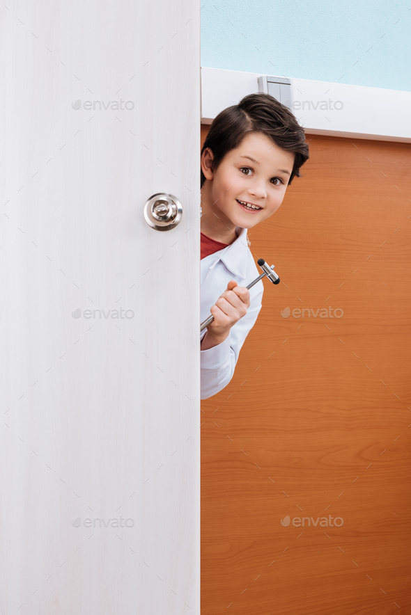 Smiling boy doctor with reflex hammer standing in doorway and looking at camera