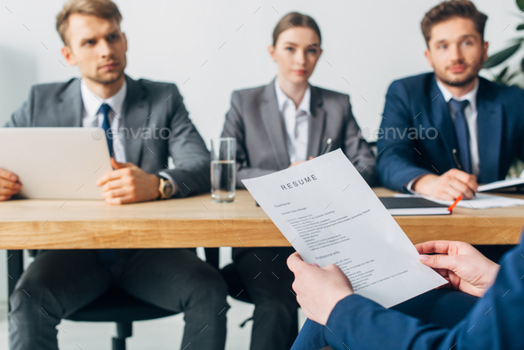 Selective focus of employee holding resume near recruiters at table in office