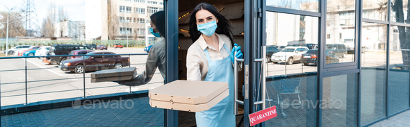 Horizontal image of cafe owner in medical mask near door with card with quarantine lettering showing
