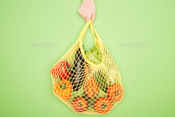 cropped view of woman holding string bag with raw vegetables
