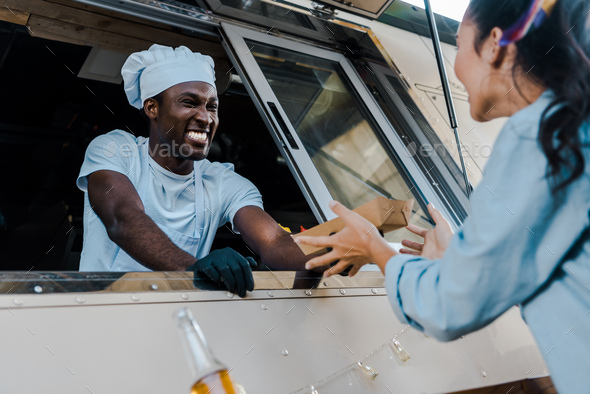 low angle view of cheerful african american man giving carton plate to customer