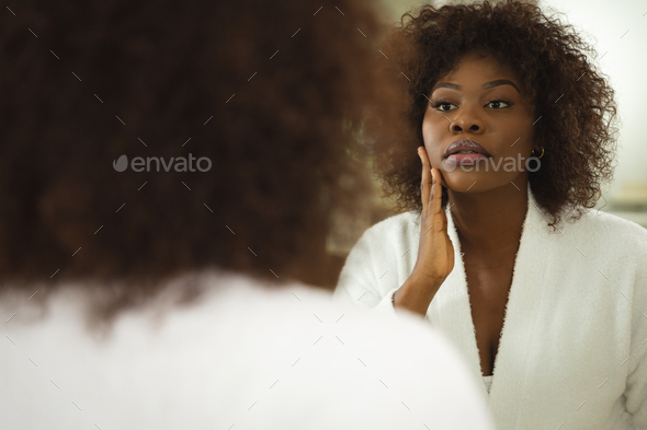 African american woman in bathroom wearing bathrobe, looking in mirror ...