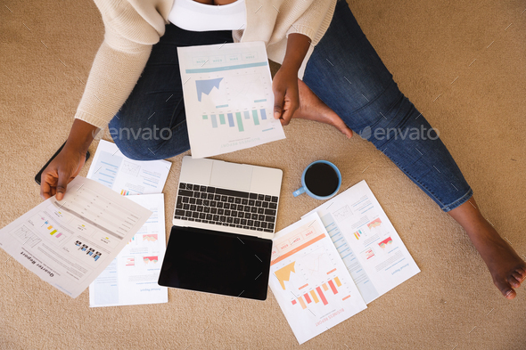 Happy african american woman working in bedroom, sitting floor using laptop and holding paperwork - Stock Photo - Images