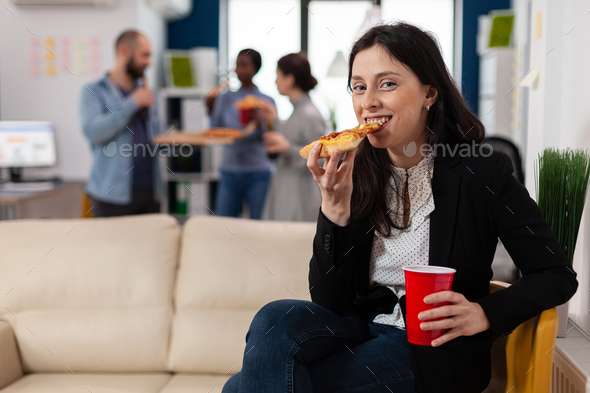 Woman eating slice of pizza at after work party with friends