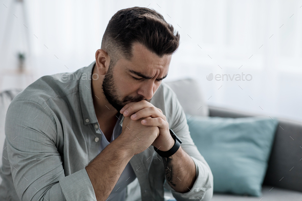 Unhappy depressed caucasian handsome bearded man crying in living room couch, feeling desperate