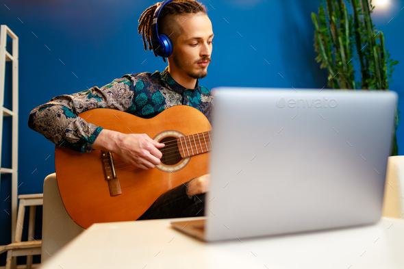 Young stylish caucasian man taking guitar class online at home using his laptop