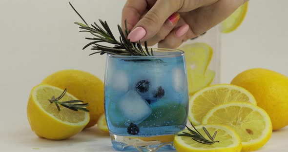 Adding Rosemary Branch in a Glass with Soda Lemonade Blue Cocktail alt