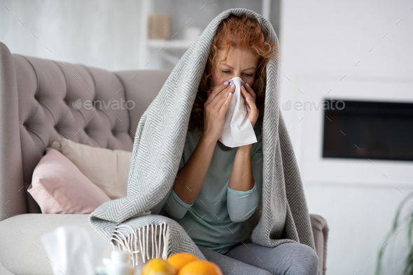 Red-haired woman using napkin while having stuff nose