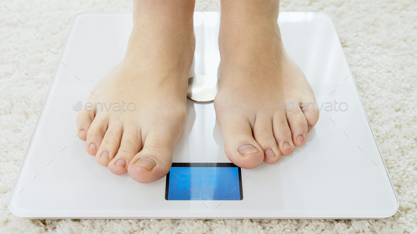 Diet. Top View Of Female Bare Feet Standing On A Scale. Caucasian Young  Woman Measuring Body Weight On Weighing Scale At Home. Weight Loss.  Dieting; Exercising. Healthy Eating; Lifestyle. Stock Photo