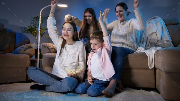 Happy cheerful family celebrating victory or football goal while watching TV at night
