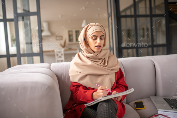 Pretty girl wearing hijab writing an article